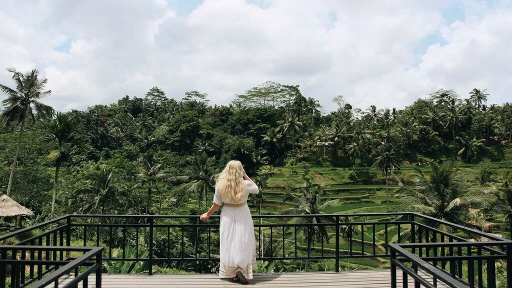 A guest overlooks lush rice terraces and tropical forest from a scenic viewpoint in Ubud, Bali.