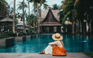 A guest relaxes beside a tranquil tropical resort pool surrounded by swaying palm trees and lush gardens.