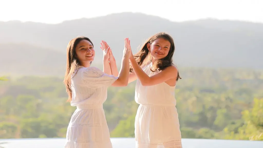 Two guests share a joyful moment beside an infinity pool overlooking lush tropical hills at sunset.