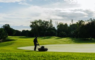A beautifully maintained golf course with manicured greens surrounded by lush tropical landscapes under a bright morning sky.