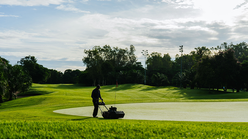 A beautifully maintained golf course with manicured greens surrounded by lush tropical landscapes under a bright morning sky.