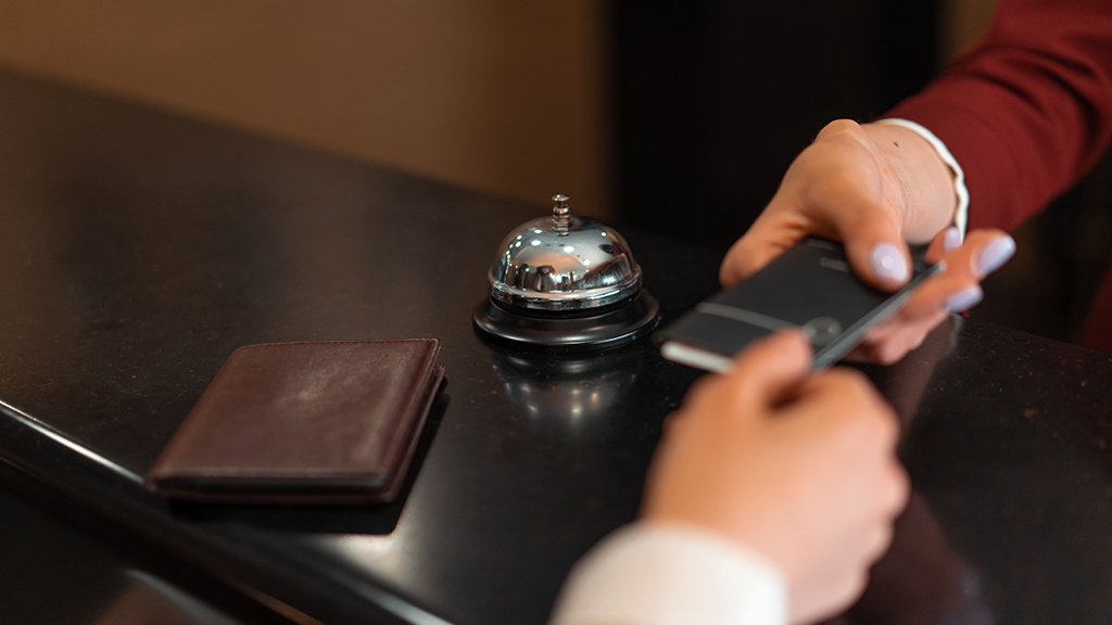 Guest checking in at a luxury hotel reception with a contactless key card beside the front desk bell.